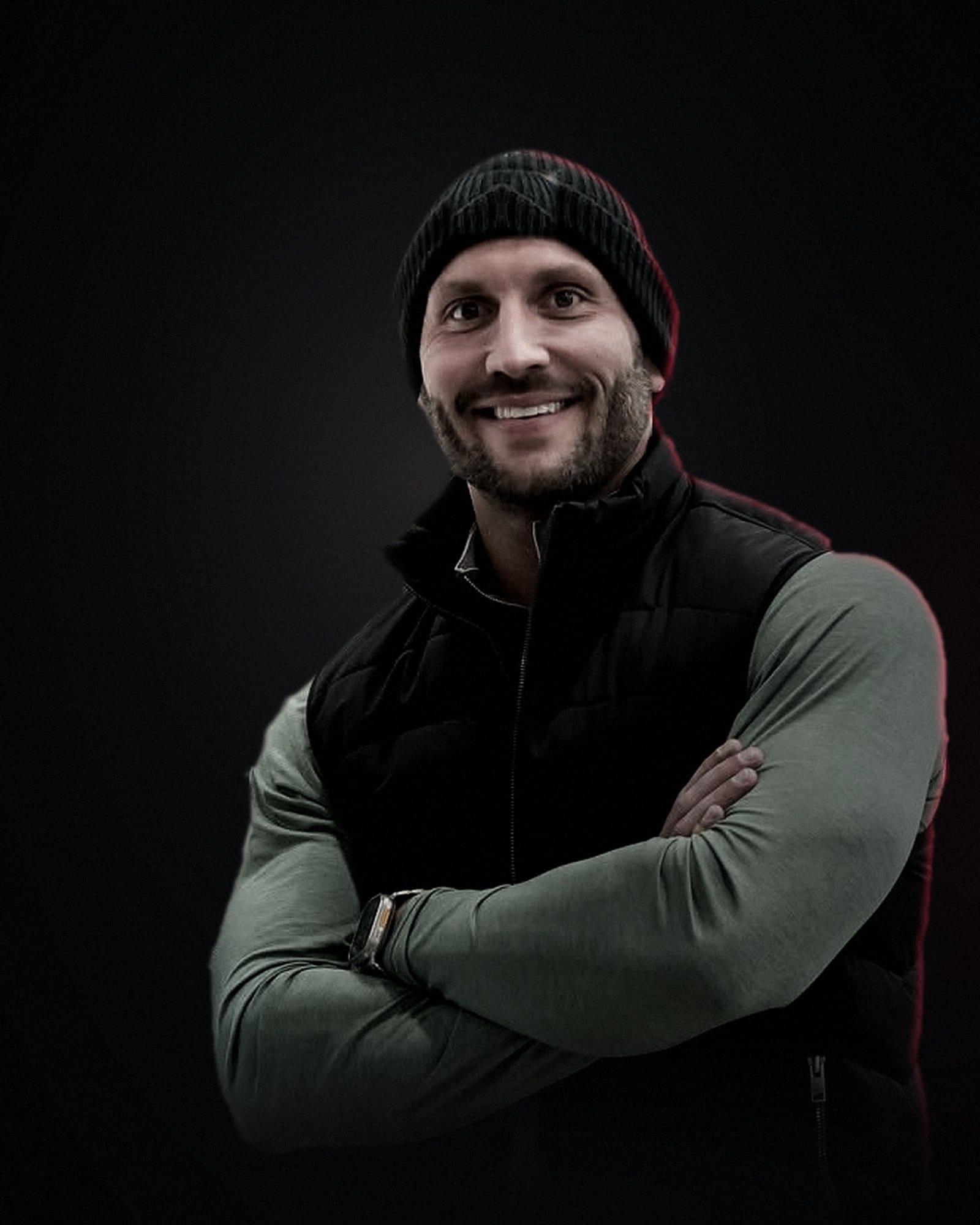 Brady Fedro, arms crossed, in a dark room lit by a single warm key light with a crimson rim.